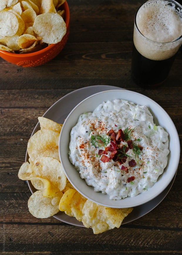 A bowl of Bacon Leek Dip, potato chips, and a glass of beer.