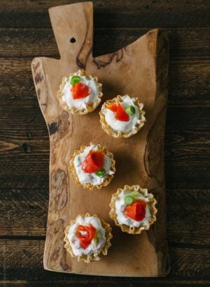 Five smoked salmon appetizer bites on a wooden serving board.