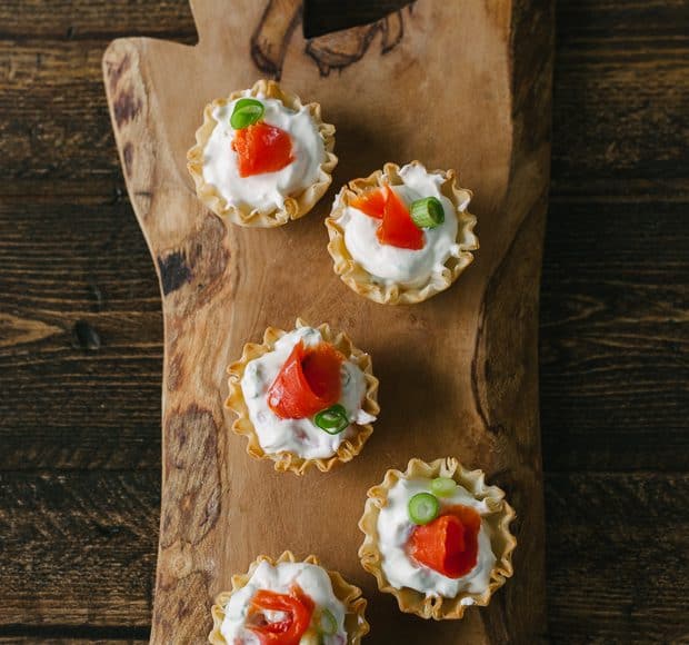 Five smoked salmon appetizer bites on a wooden serving board.