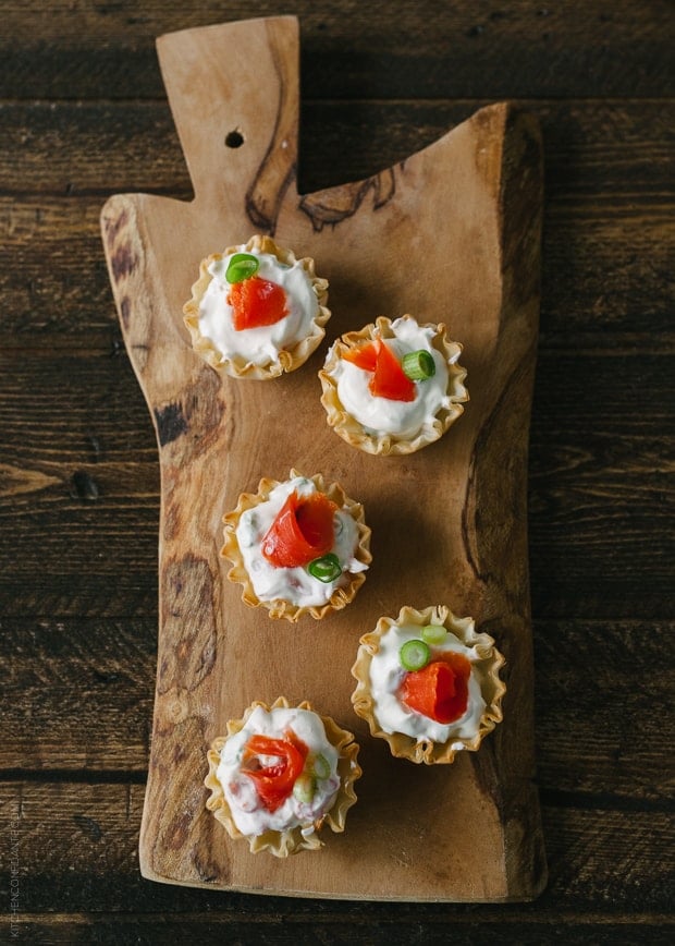 Five smoked salmon appetizer bites on a wooden serving board.