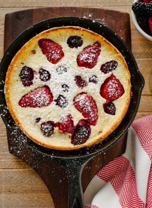 A Dutch Baby Pancake in cast iron pan with strawberries and blackberries baked into the top.