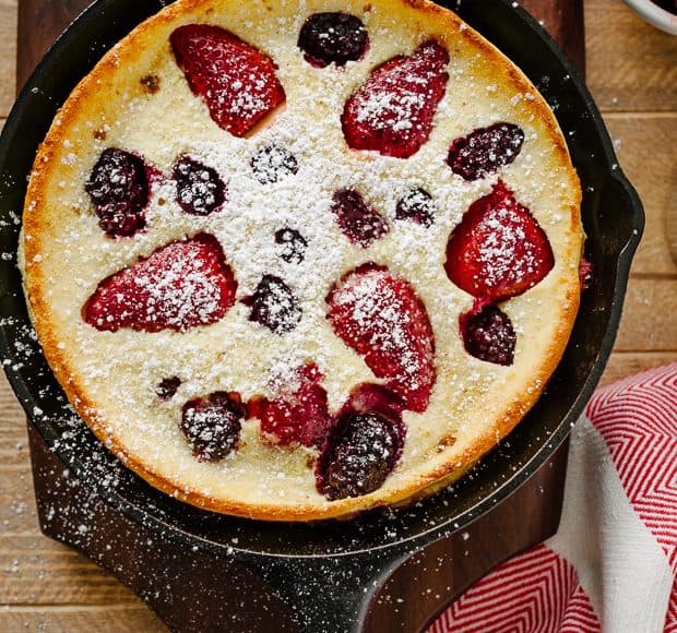 A Dutch Baby Pancake in cast iron pan with strawberries and blackberries baked into the top.