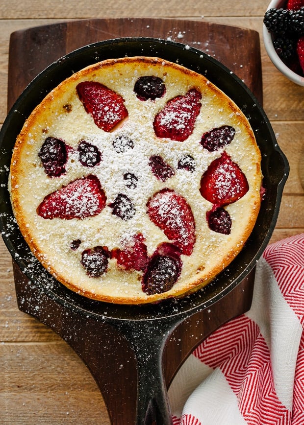 A Dutch Baby Pancake in cast iron pan with strawberries and blackberries baked into the top.