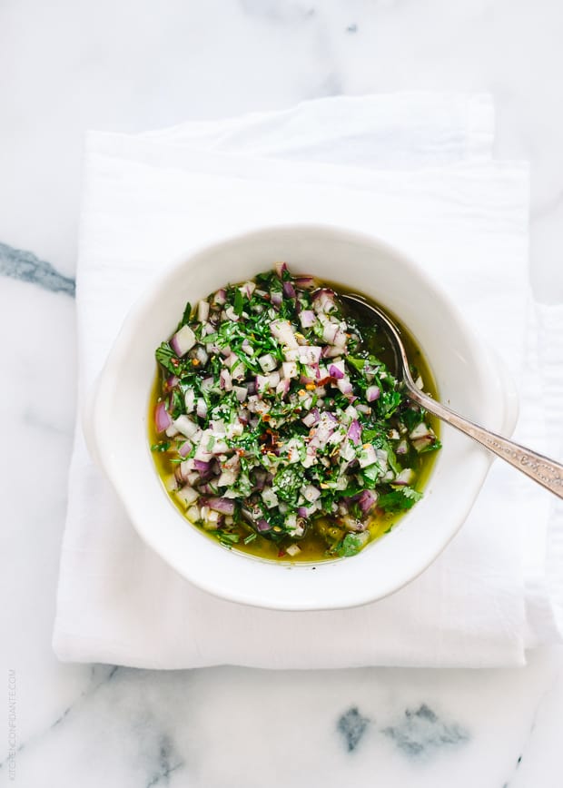A white bowl filled with colorful green Chimichurri Sauce.