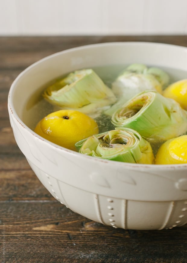 Artichokes soaking in water with lemons.