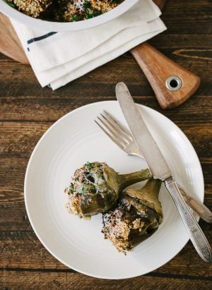 Two Toasted Quinoa Stuffed Artichokes arranged on a white plate.