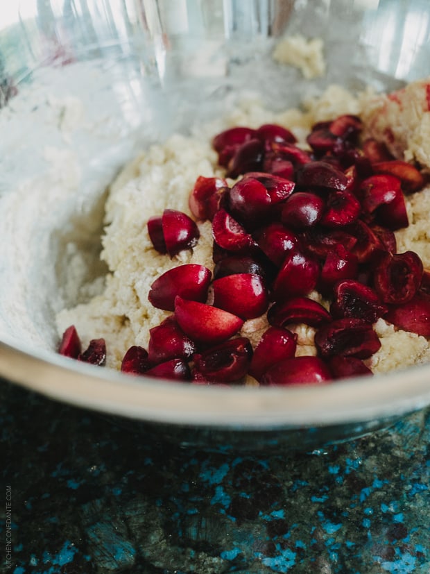 Quartered cherries added to a bowl of dough for scones.