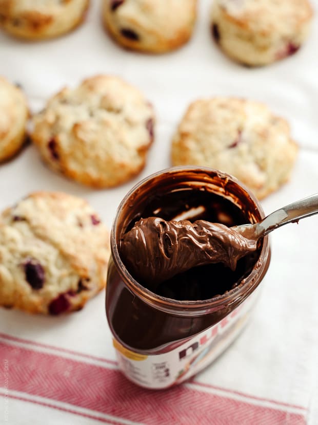 Scooping out Nutella from the jar with Cherry Nutella Scones in the background.