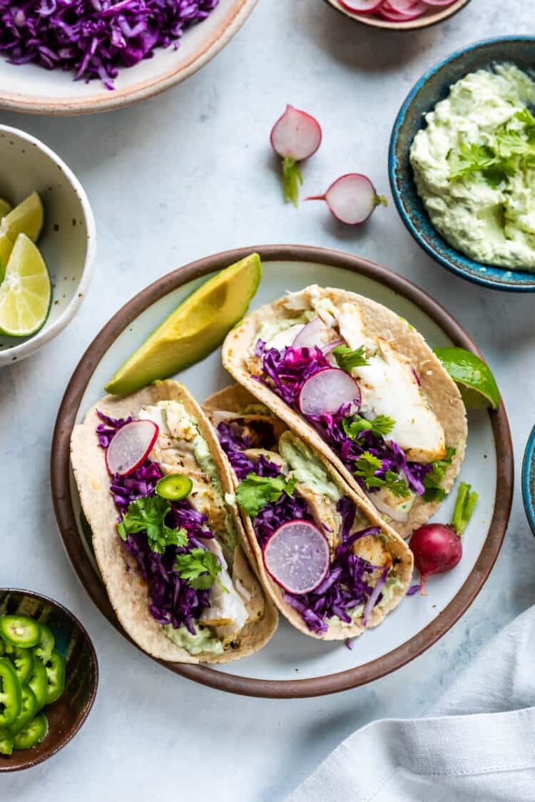 Grilled Fish Tacos with Avocado-Cilantro Sauce on a plate garnished with red cabbage, radishes and jalapeño.