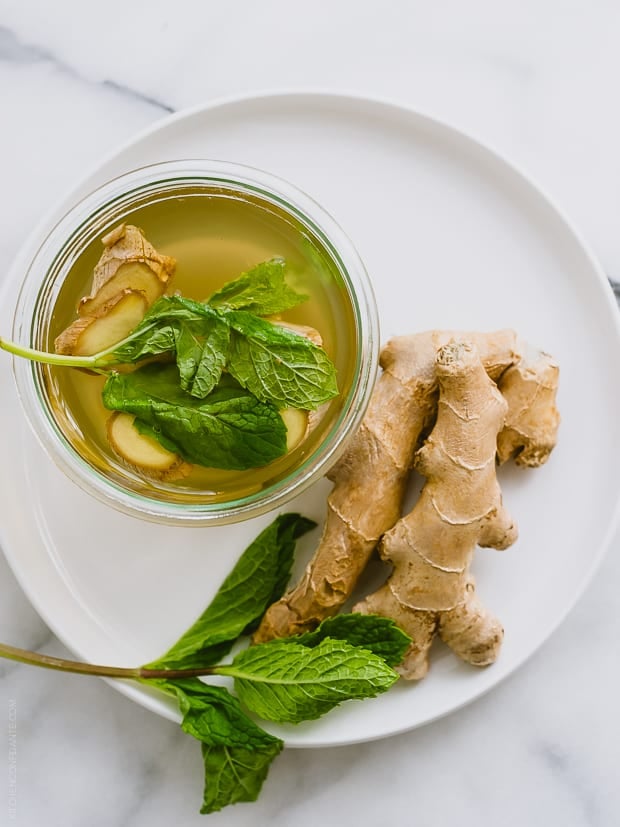 The top of a ginger-mint cooler alongside fresh ginger on a white plate.