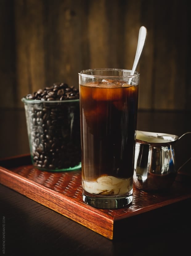 A glass of Homemade Thai Iced Coffee with coffee beans in the background.