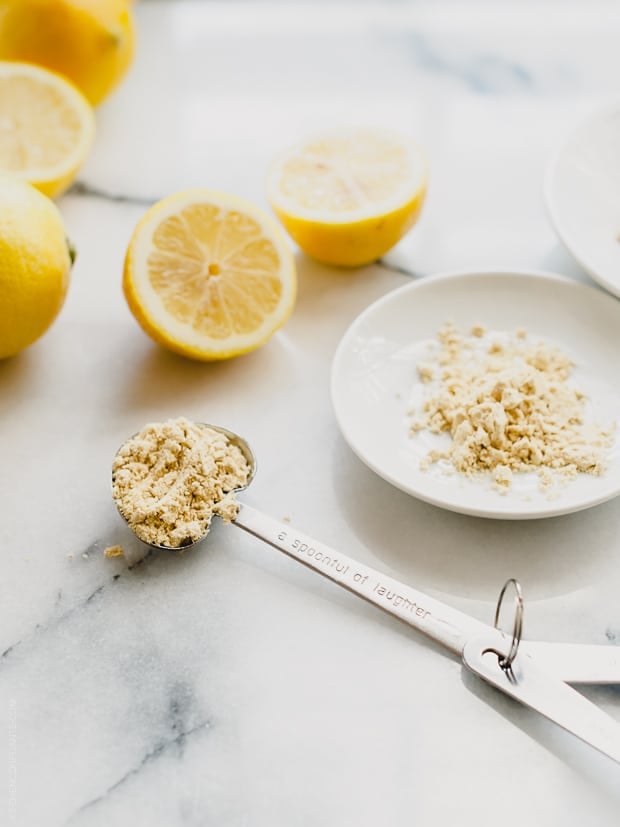 Halved lemons and a heart-shaped teaspoon measuring out ginger on a marble surface.