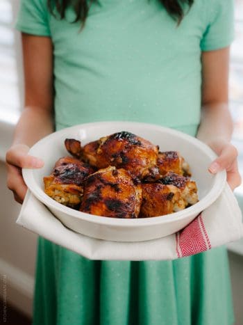 A girl holding a large white platter of Honey Spice Marinated Grilled Chicken.