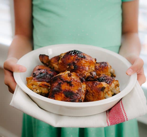 A girl holding a large white platter of Honey Spice Marinated Grilled Chicken.