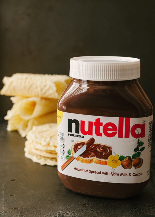 A jar of Nutella with pizzelle in the background.