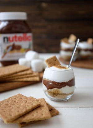 A Nutella S'mores Parfait surrounded by graham crackers and a jar of Nutella.