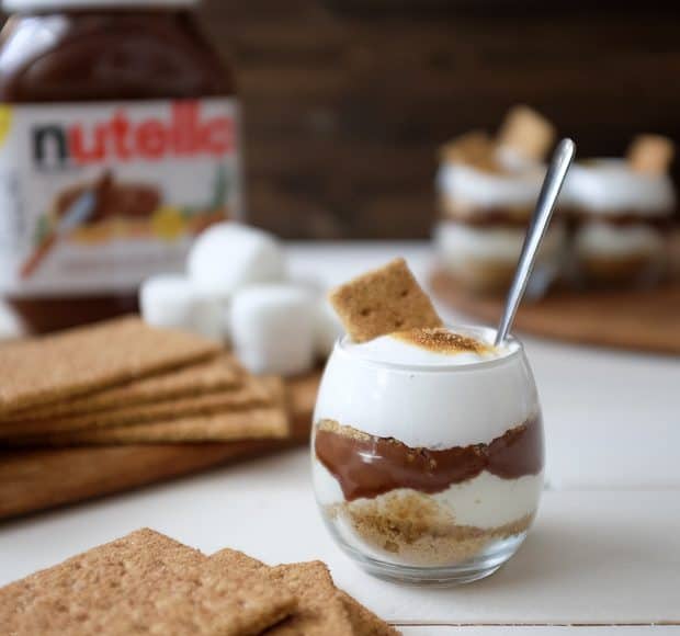 A Nutella S'mores Parfait surrounded by graham crackers and a jar of Nutella.