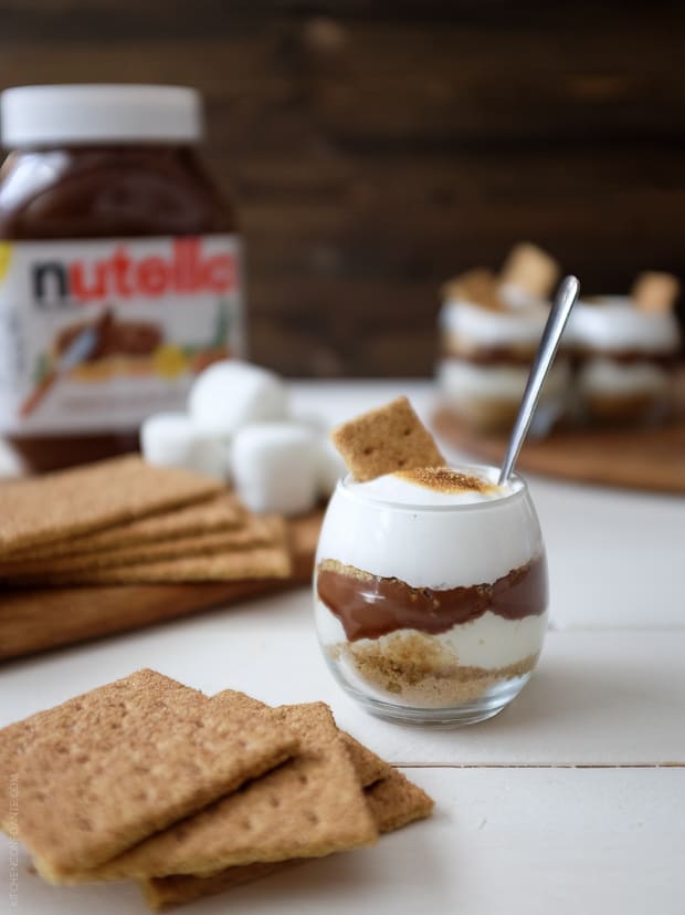 A Nutella S'mores Parfait surrounded by graham crackers and a jar of Nutella.