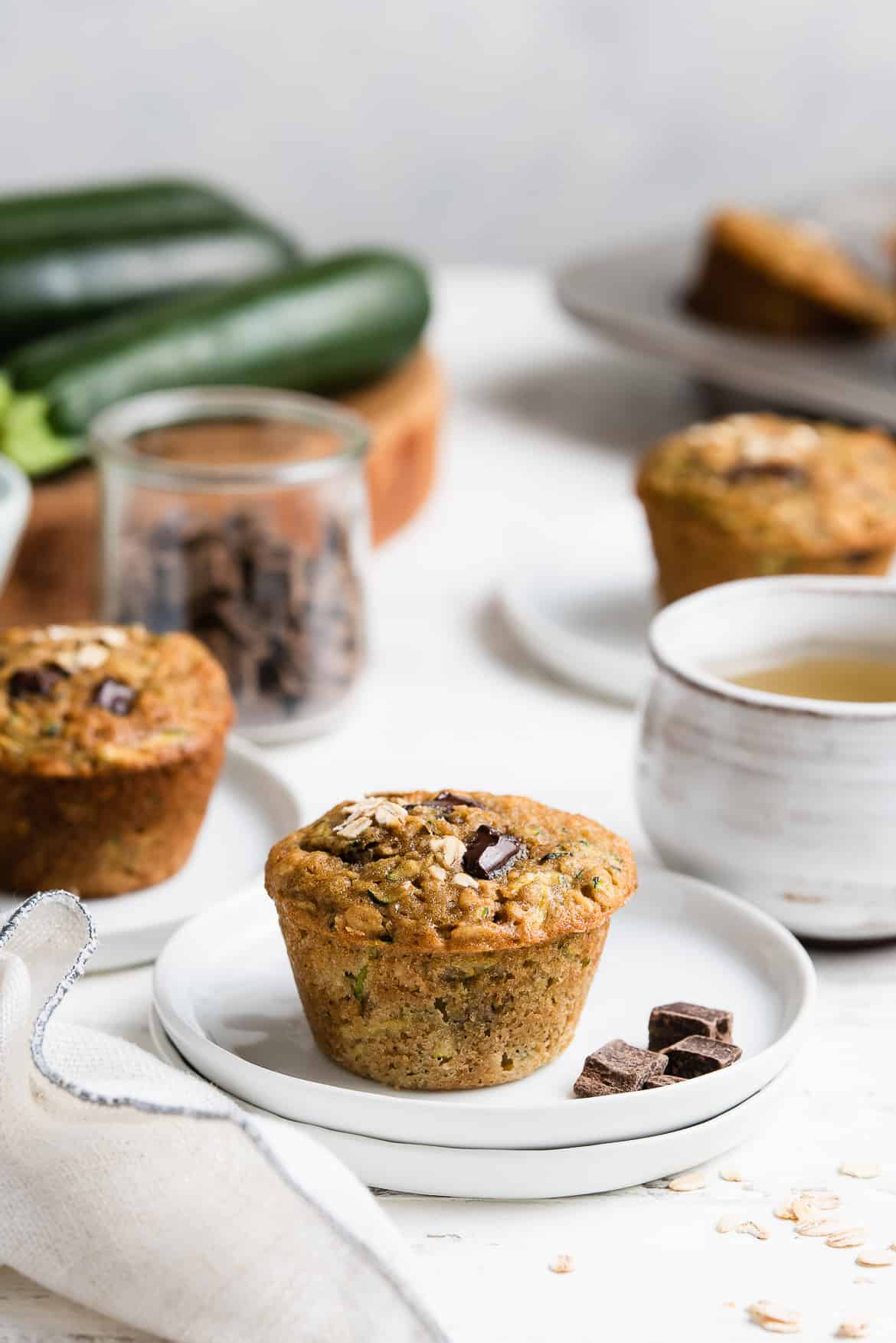 Zucchini Oat Chocolate Chunk Muffins on small white plates with a cup of tea.