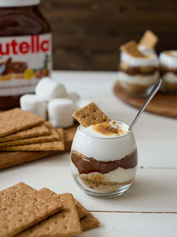 A Nutella S'mores Parfait surrounded by graham crackers and a jar of Nutella.