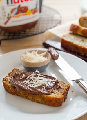 A slice of Coconut Banana Bread on a white plate spread with Nutella.