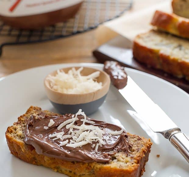 A slice of Coconut Banana Bread on a white plate spread with Nutella.