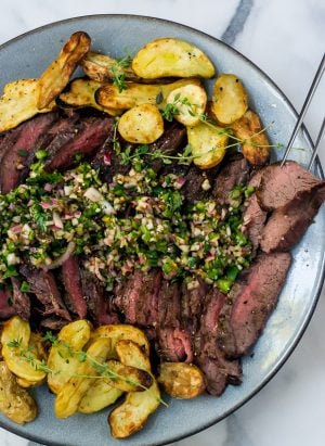Sliced grilled flank steak surrounded by grilled fingerling potatoes and topped with chimichurri sauce.