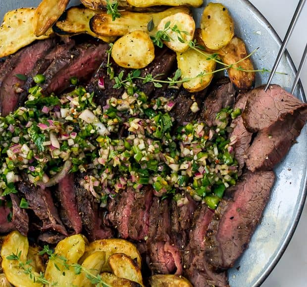 Sliced grilled flank steak surrounded by grilled fingerling potatoes and topped with chimichurri sauce.