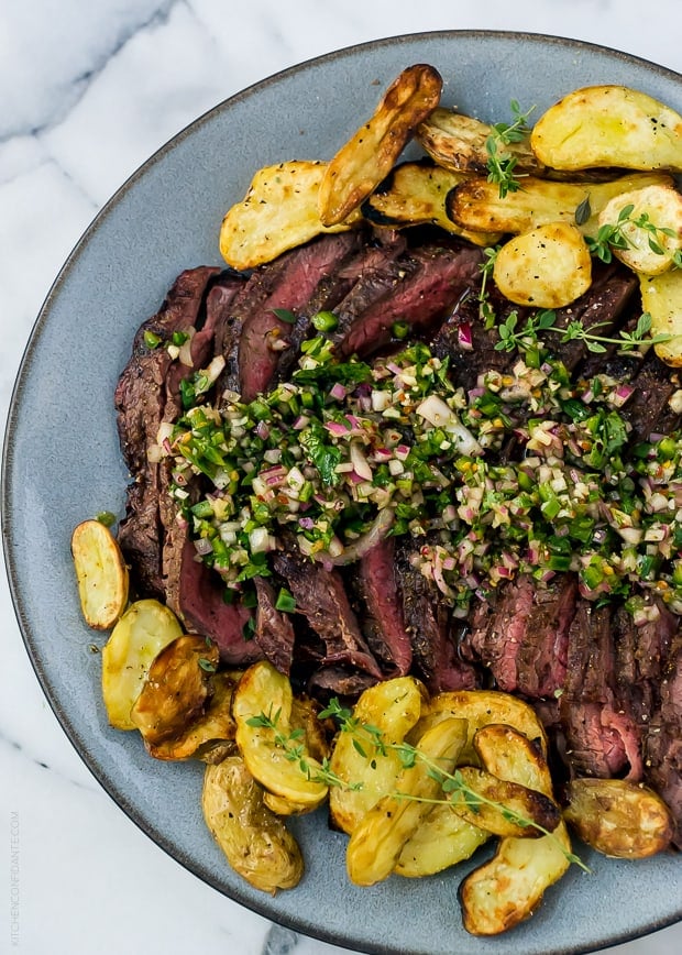 Sliced grilled flank steak surrounded by grilled fingerling potatoes and topped with chimichurri sauce.
