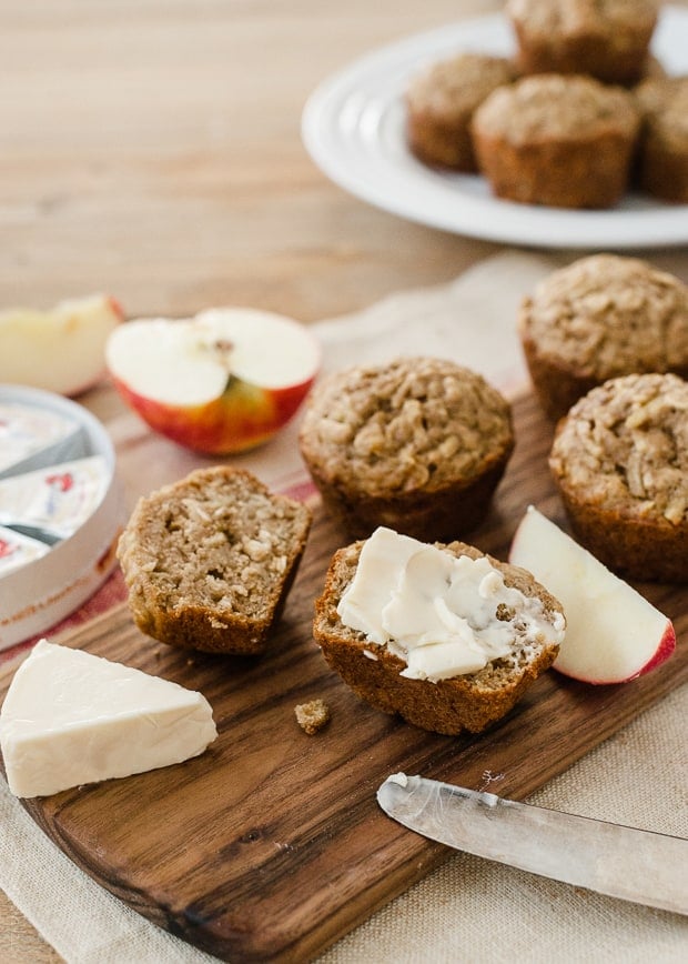 Muffins halved and spread with a creamy cheese on a wooden serving board.