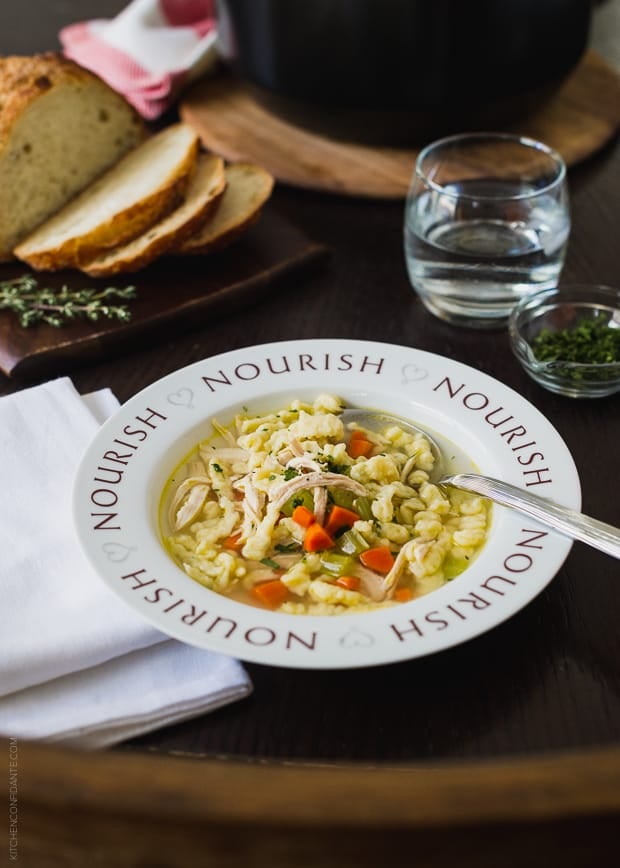 Chicken and Herb Spaetzle Soup served in a bowl with the word, “Nourish” around the rim.