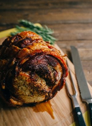 Golden brown Porchetta on a wooden board with carving utensils nearby.