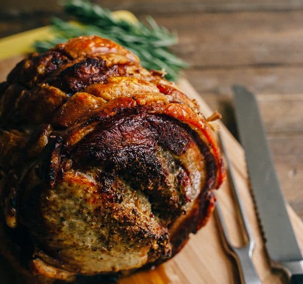 Golden brown Porchetta on a wooden board with carving utensils nearby.