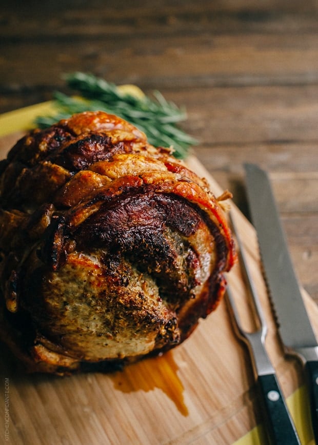 Golden brown Porchetta on a wooden board with carving utensils nearby.