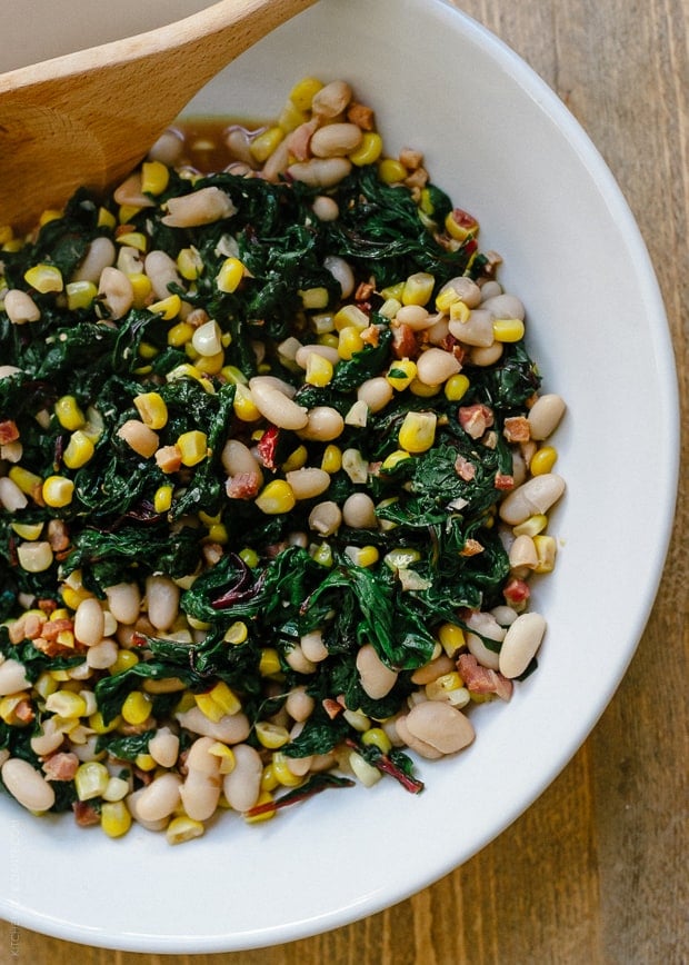 A white bowl filled with Swiss Chard with Pancetta, Corn and Cannelini Beans.