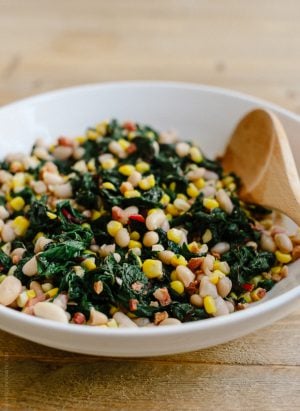 A white bowl filled with Swiss Chard with Pancetta, Corn and Cannelini Beans.
