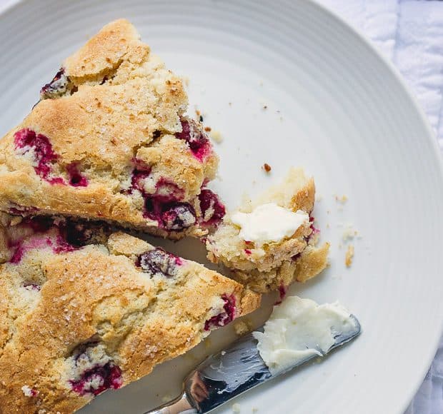Two Make-Ahead Cranberry Scones on a white plate alongside a buttered knife.