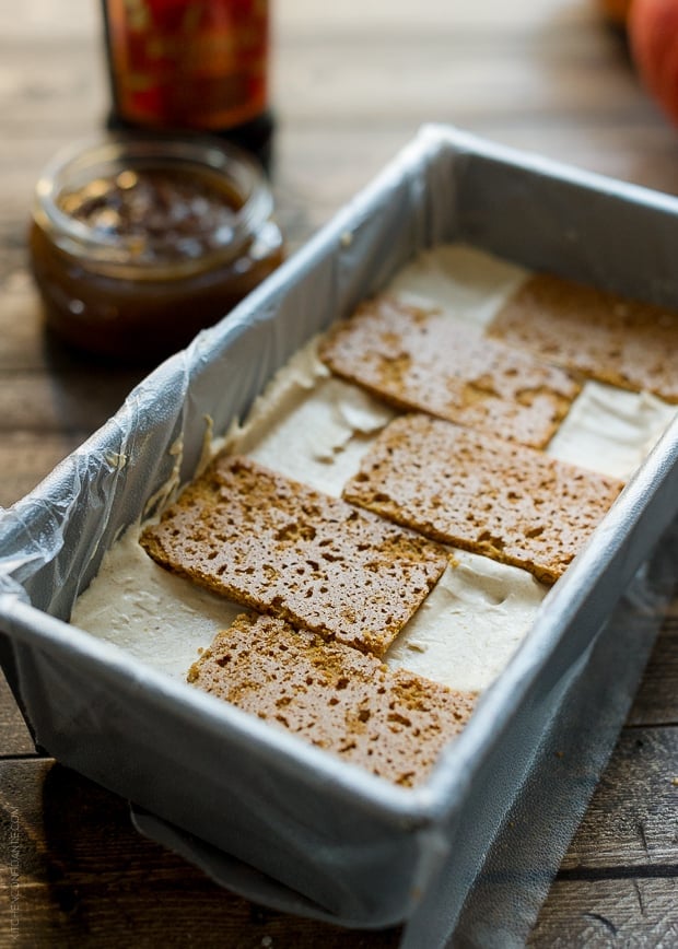 Layers of graham crackers on top of pumpkin spice mascarpone cream in a lined loaf pan.