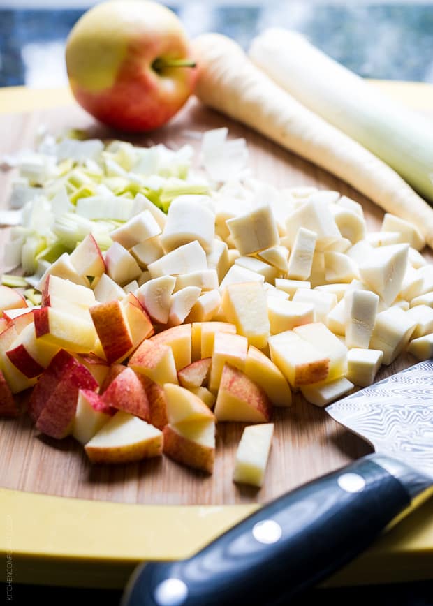 Chopped apples, parsnips, and leeks on a wooden surface.