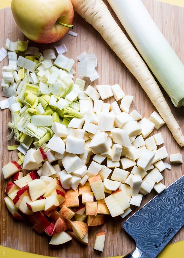 Chopped apples, leeks, and parsnips on a wooden surface.