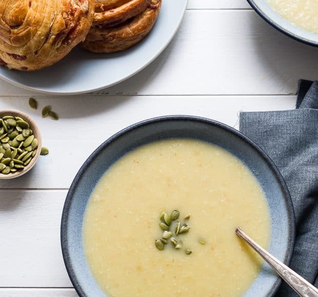 A bowl of creamy colored Parsnip Apple Soup on a wooden surface.