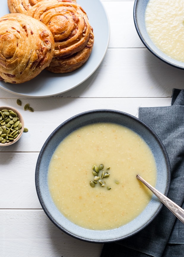 A bowl of creamy colored Parsnip Apple Soup on a wooden surface.