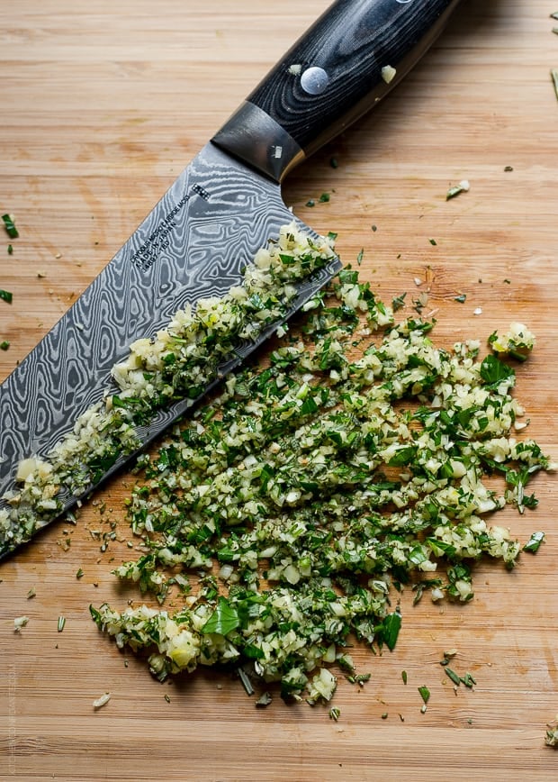 Garlic and fresh herbs chopped on a wooden surface.