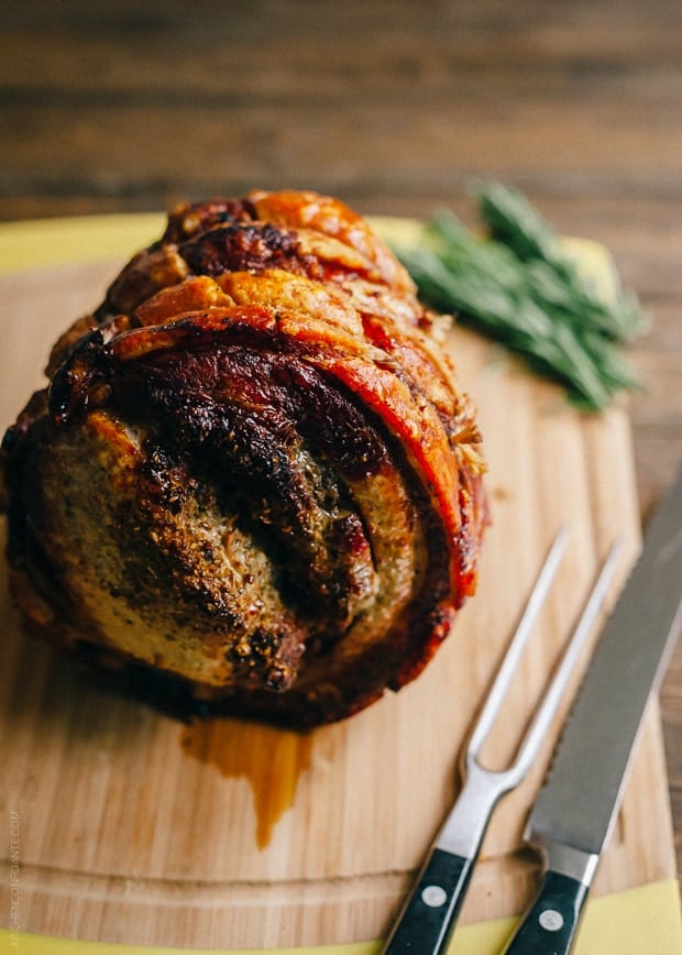 Homemade Porchetta on wooden surface with carving utensils nearby.