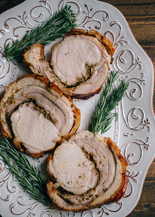 Slices of porchetta on a decorative serving platter with sprigs of rosemary to garnish.