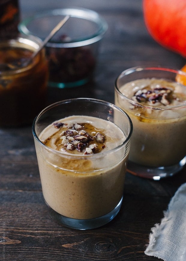 Two glasses filled with Pumpkin Butter Smoothie and topped with a drizzle of honey and candied pecans.