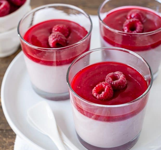 A white plate holding three glass dishes of layered raspberry panna cotta.