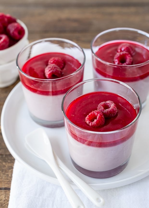 A white plate holding three glass dishes of layered raspberry panna cotta.