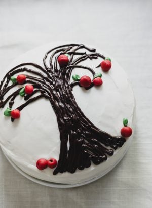 A Sweet Potato Apple Cake decorated with white icing and an apple tree design.