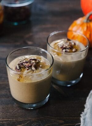 Two glasses filled with Pumpkin Butter Smoothie and topped with a drizzle of honey and candied pecans.